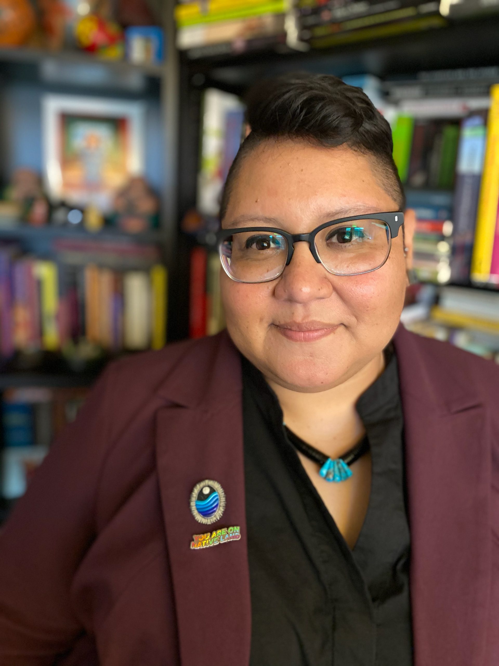 Headshot of Dr. Elisa Diana Huerta, smiling, wearing glasses, a black shirt, and a maroon blazer.