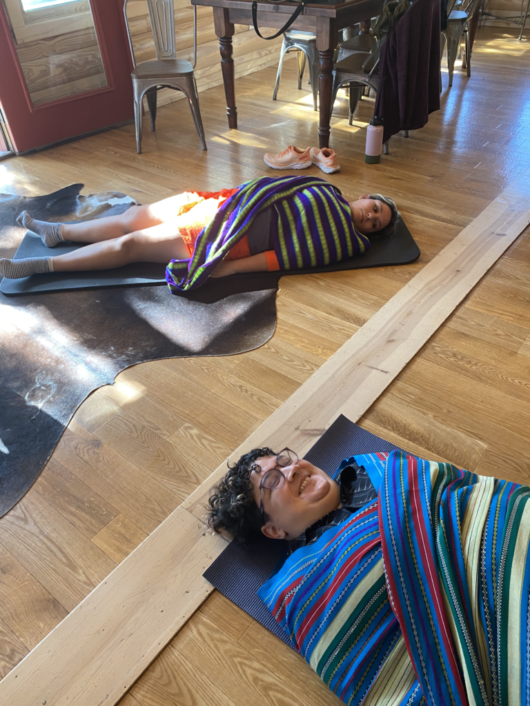 Two Florecemos participants are laying on yoga mats wrapped in blankets and smiling. 