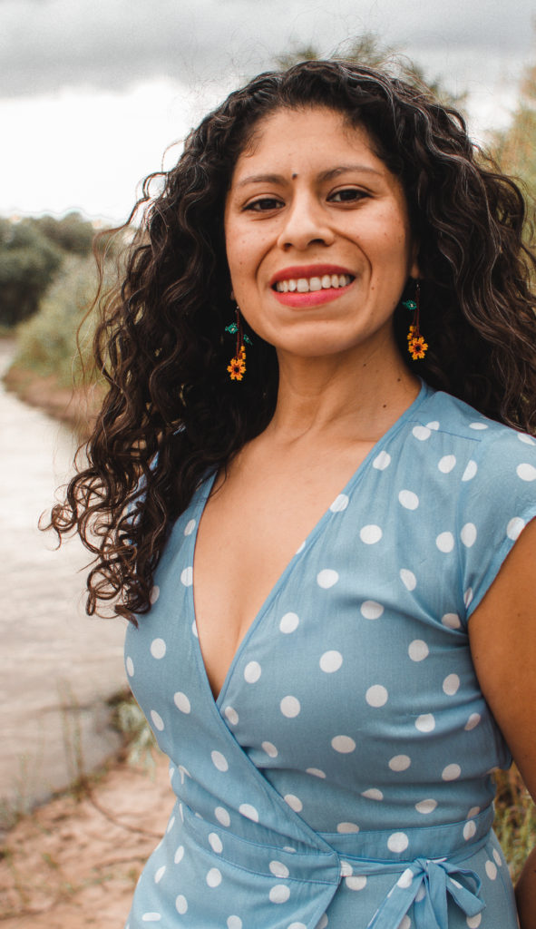 Tannia Esparza smiling with curly hair, earrings, and a blue and white polkadot dress